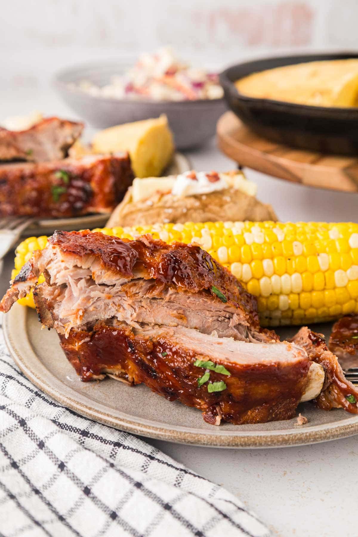 A plate of ribs with corn and baked potato.