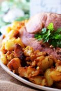 a closeup of this baked ham over roasted potatoes served for Easter