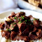 A white plate filled with white rice and this instant pot beef tips recipe aka pressure cooker beef tips garnished with chopped parsley
