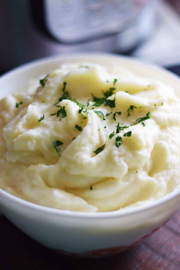 a closeup of creamy, smooth mashed potatoes in a white bowl with chopped parsley for this instant pot mashed potatoes recipe
