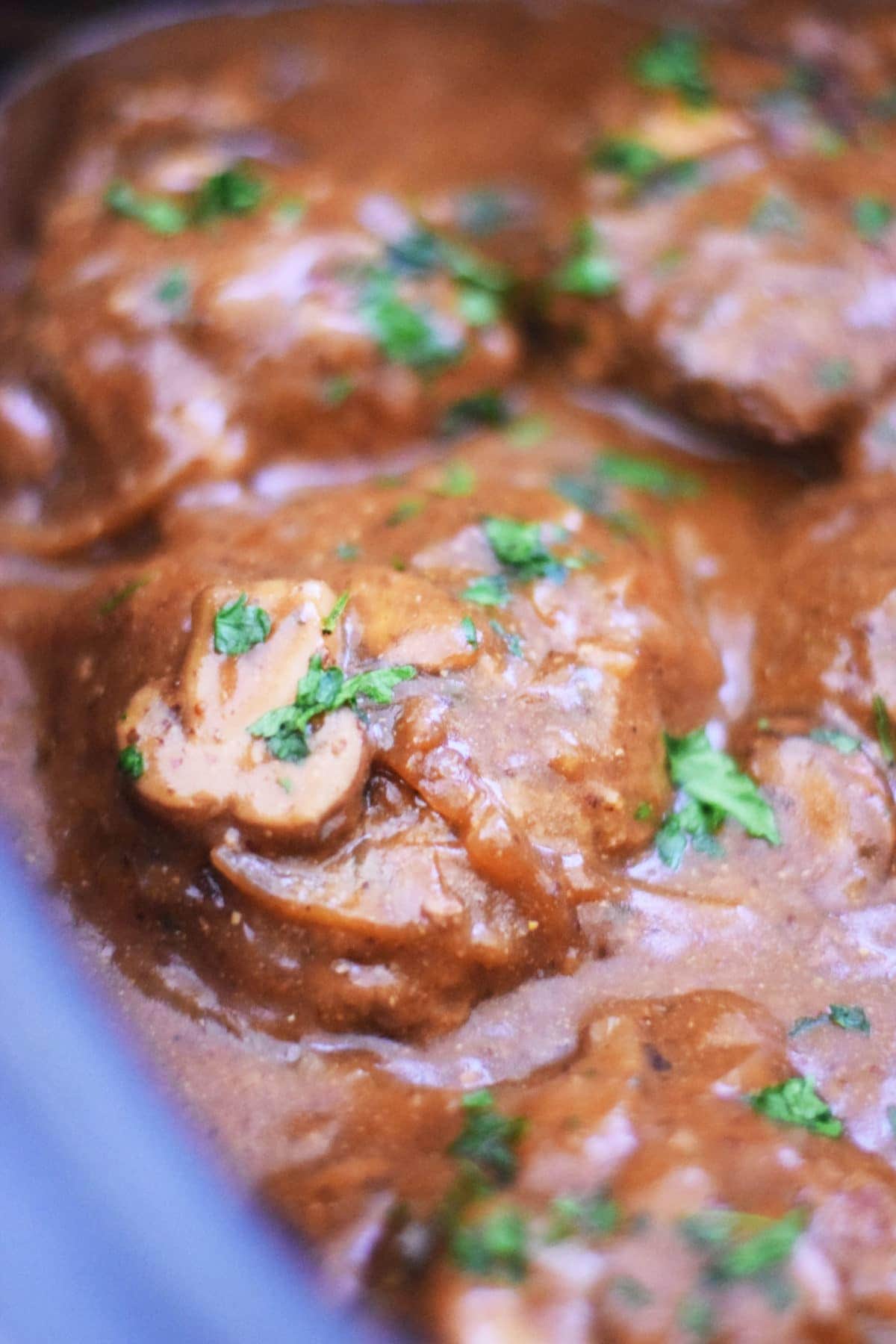 a closeup of this slow cooker salisbury steak recipe with mushrooms, gravy, and chopped parsley