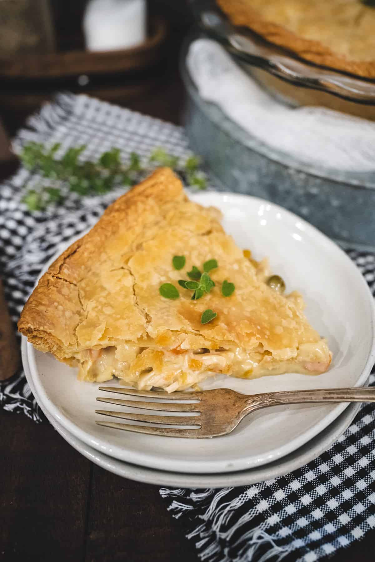 Overhead image of a whole chicken pot pie garnished with fresh thyme set on a wooden tablescape with a black and white checked placemat.