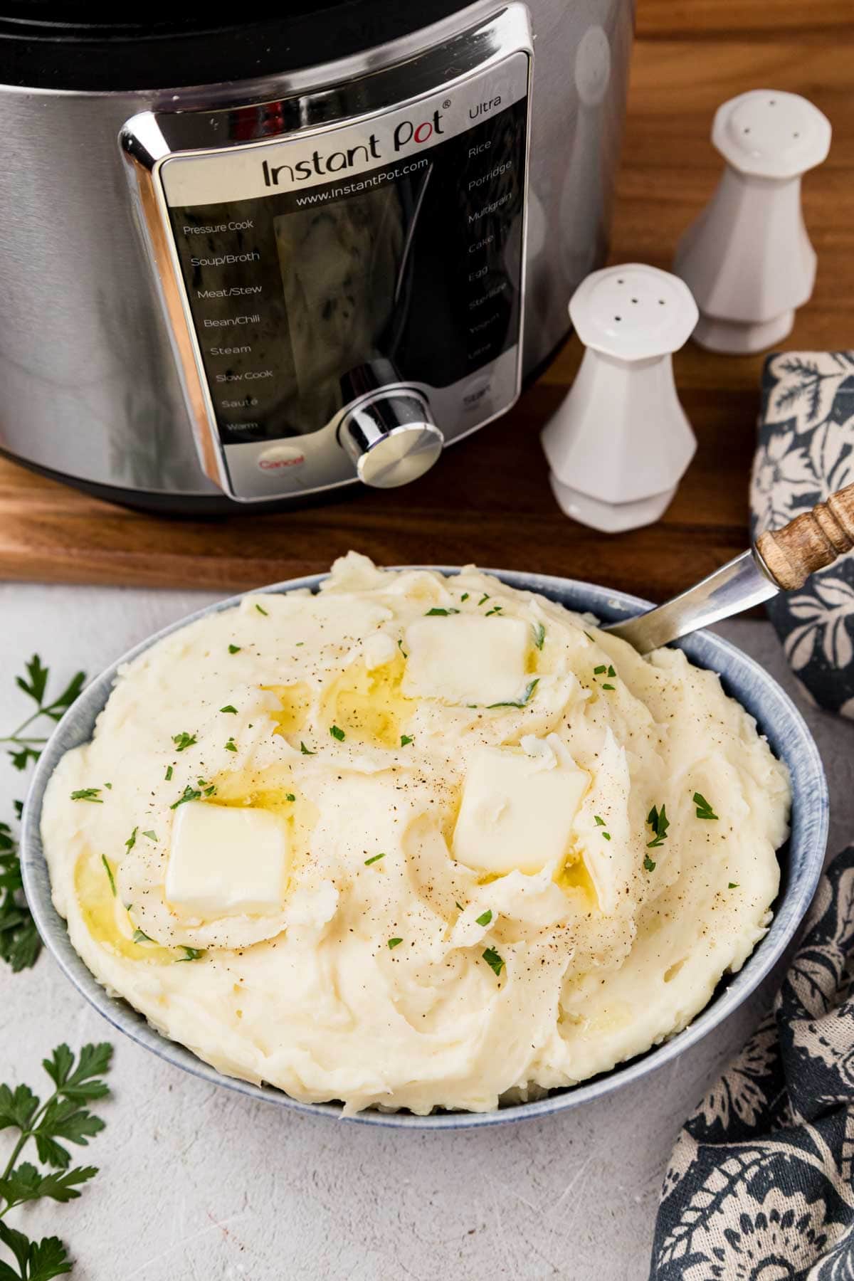 Instant Pot Mashed Potatoes A bowl of creamy Instant pot mashed potatoes with the Instant Pot in the background.