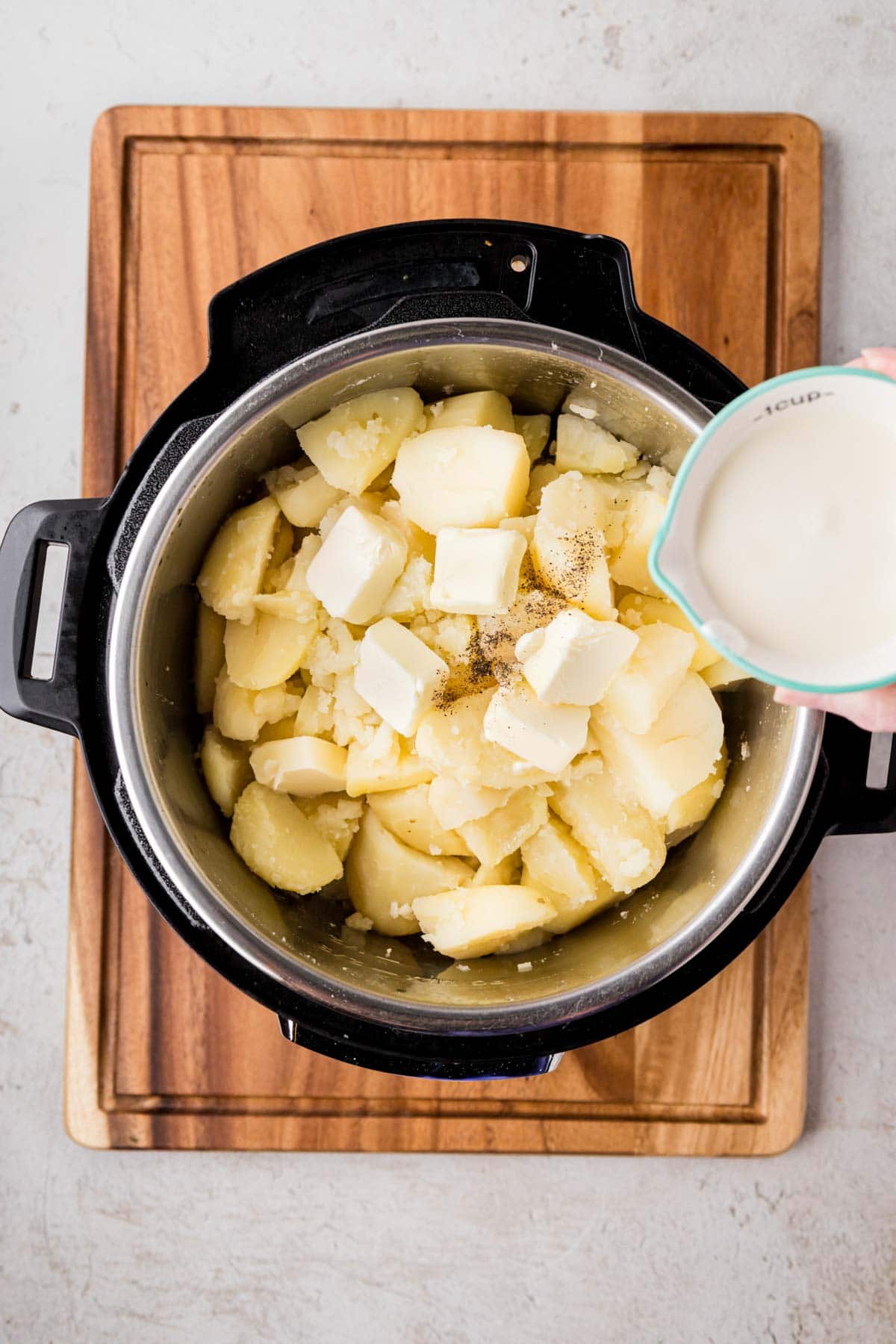 Adding heavy cream, butter and salt and pepper into the instant pot with the cooked and drained potatoes.