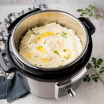 An Instant Pot filled with creamy mashed potatoes and garnished with butter and parsley.