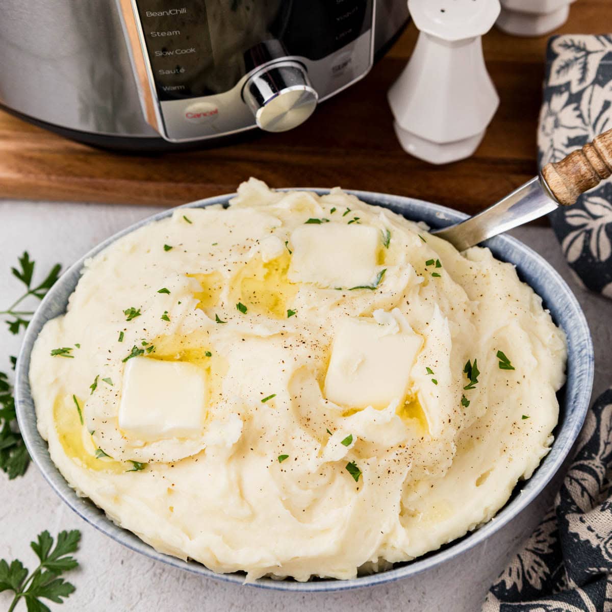 A bowl of creamy Instant pot mashed potatoes with the Instant Pot in the background.