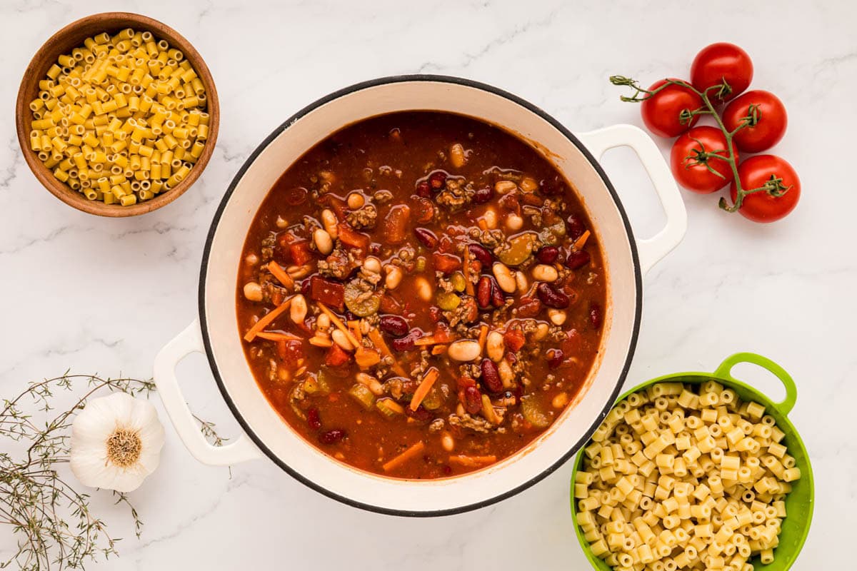 A pot of pasta e fagioli soup on a table with the colander of cooked ditalini pasta .