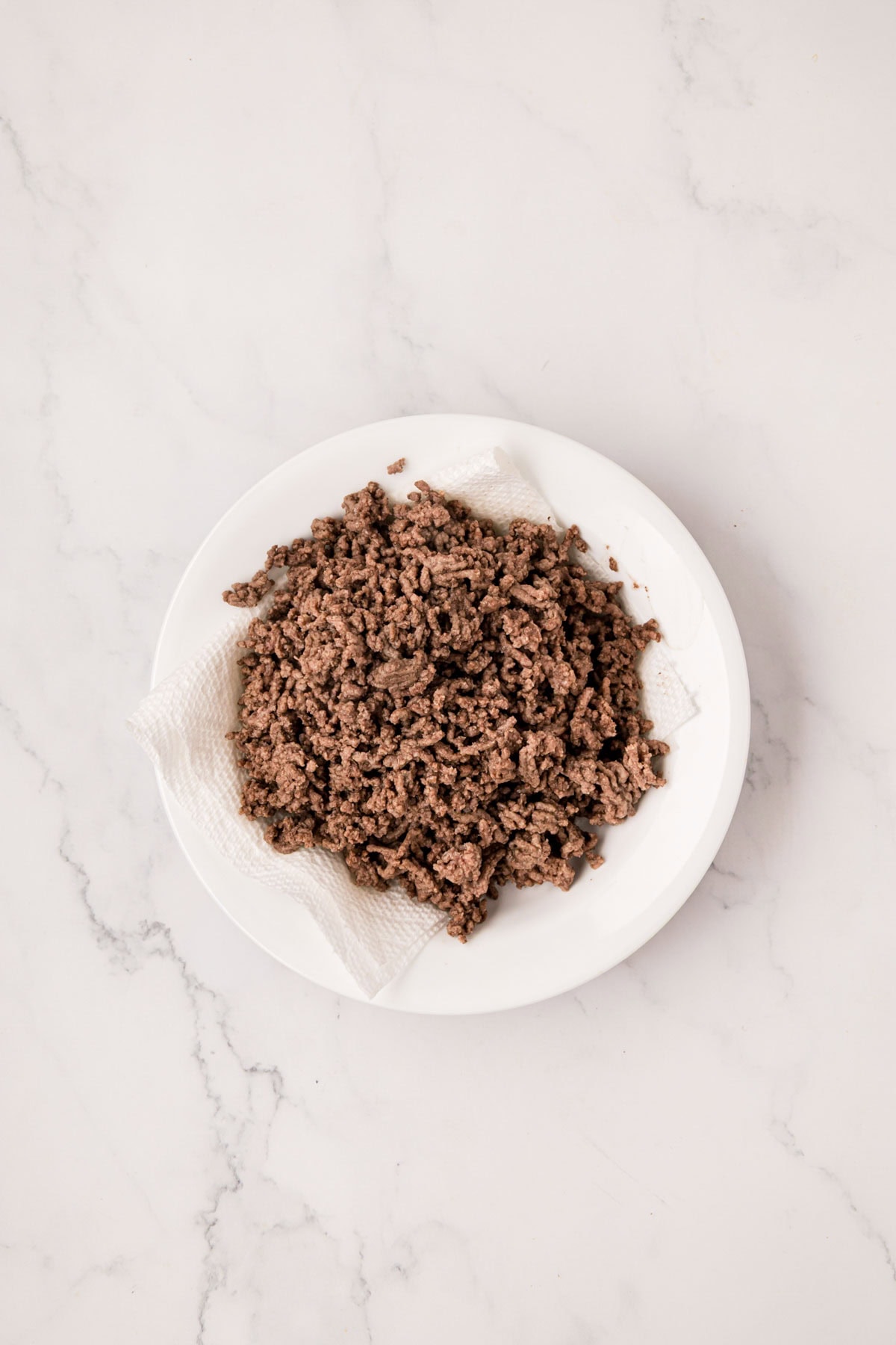 Ground beef draining grease on a paper towel lined plate.
