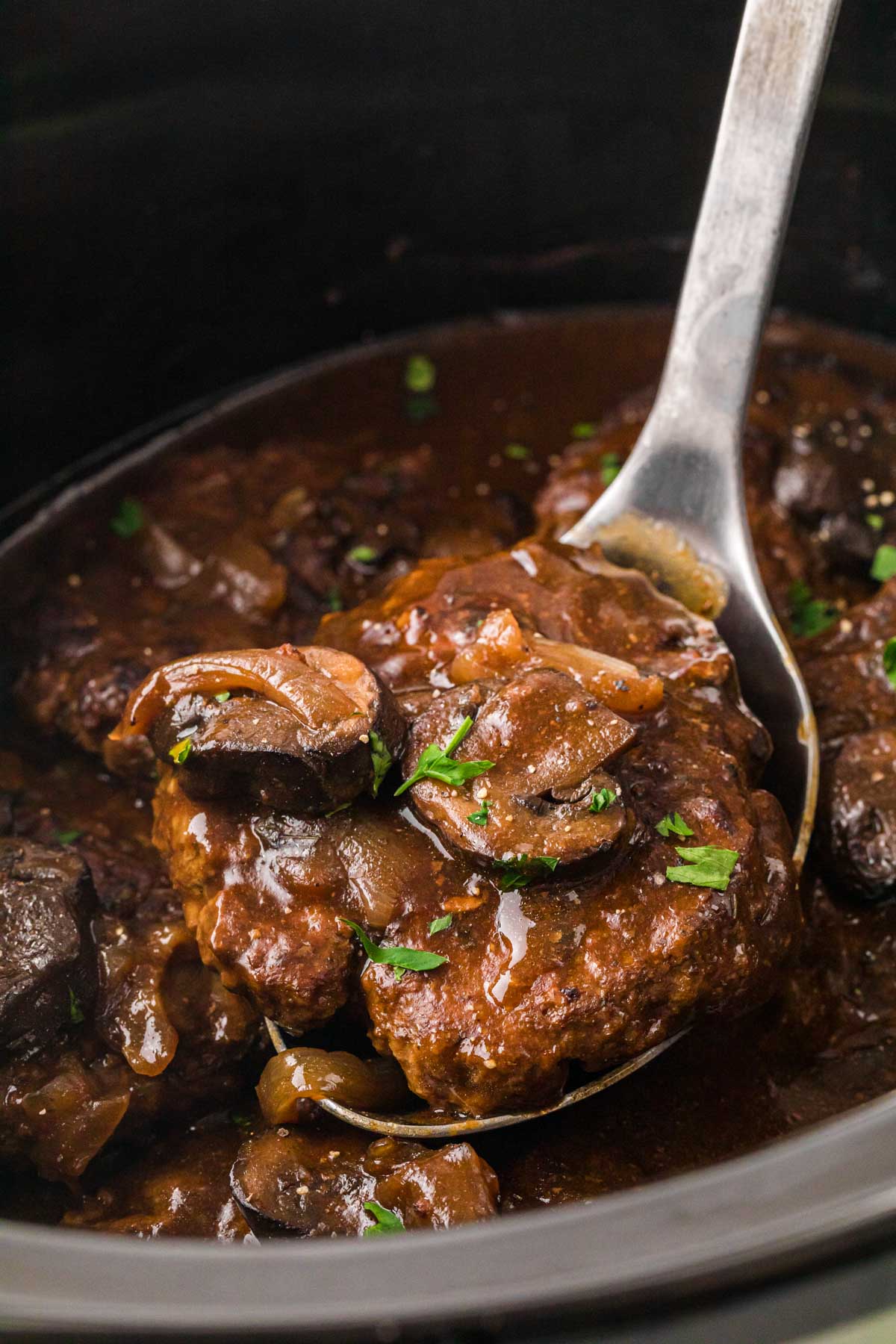 Scooping a Salisbury steak with a serving spoon out of the crockpot.