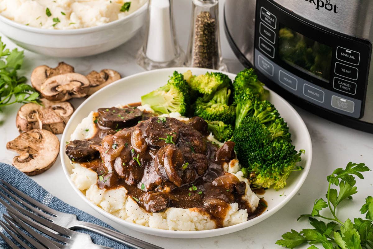 Salisbury steak over mashed potatoes served with broccoli on a white dinner plate.