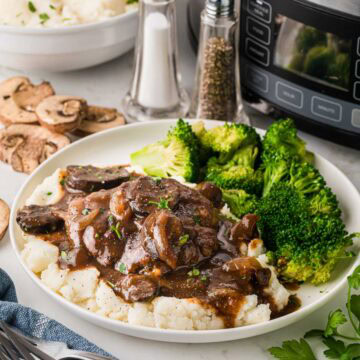 Slow Cooker Salisbury steak over mashed potatoes served with broccoli on a white dinner plate.