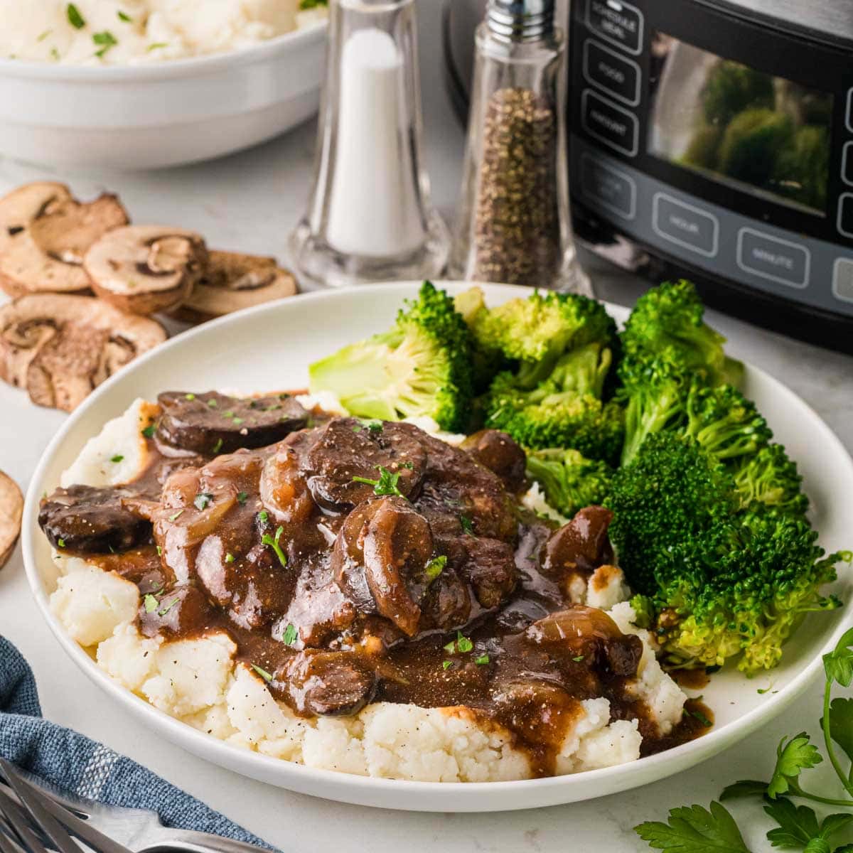 Slow Cooker Salisbury steak over mashed potatoes served with broccoli on a white dinner plate.