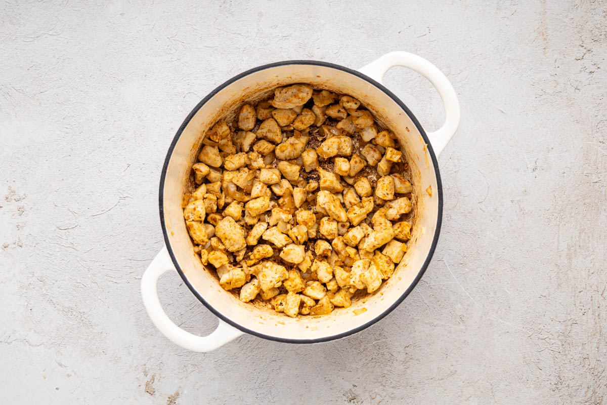 Cooked diced chicken seasoned with fajita seasoning in a dutch oven.