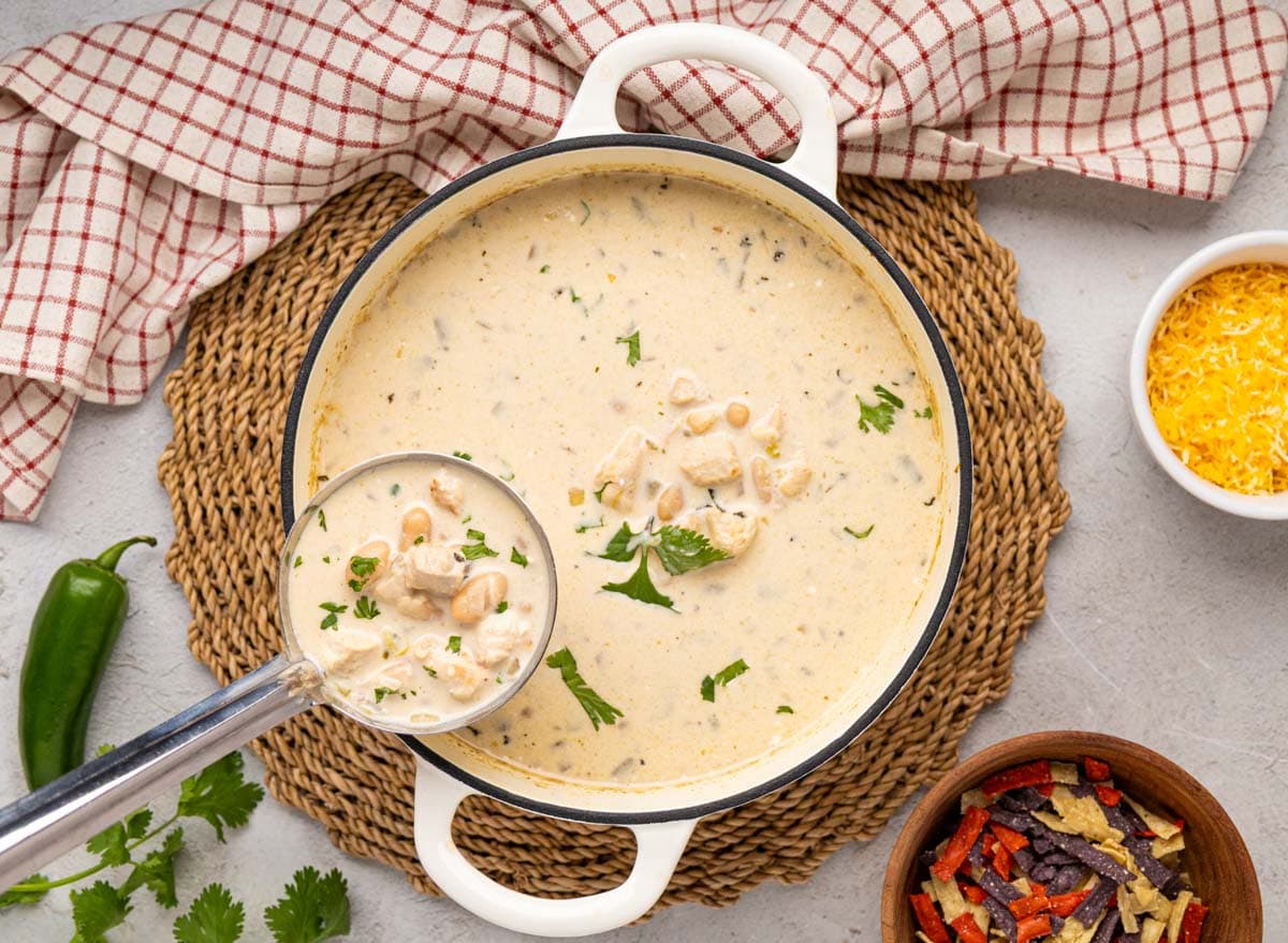 A ladle removing a scoop of white chicken chili from a white dutch oven.