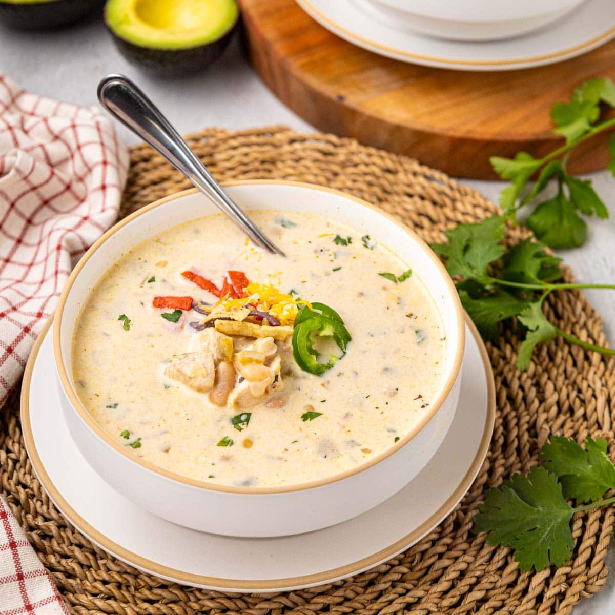 A bowl of white chicken chili topped with slice jalapeños, cheese, and tortilla strips.