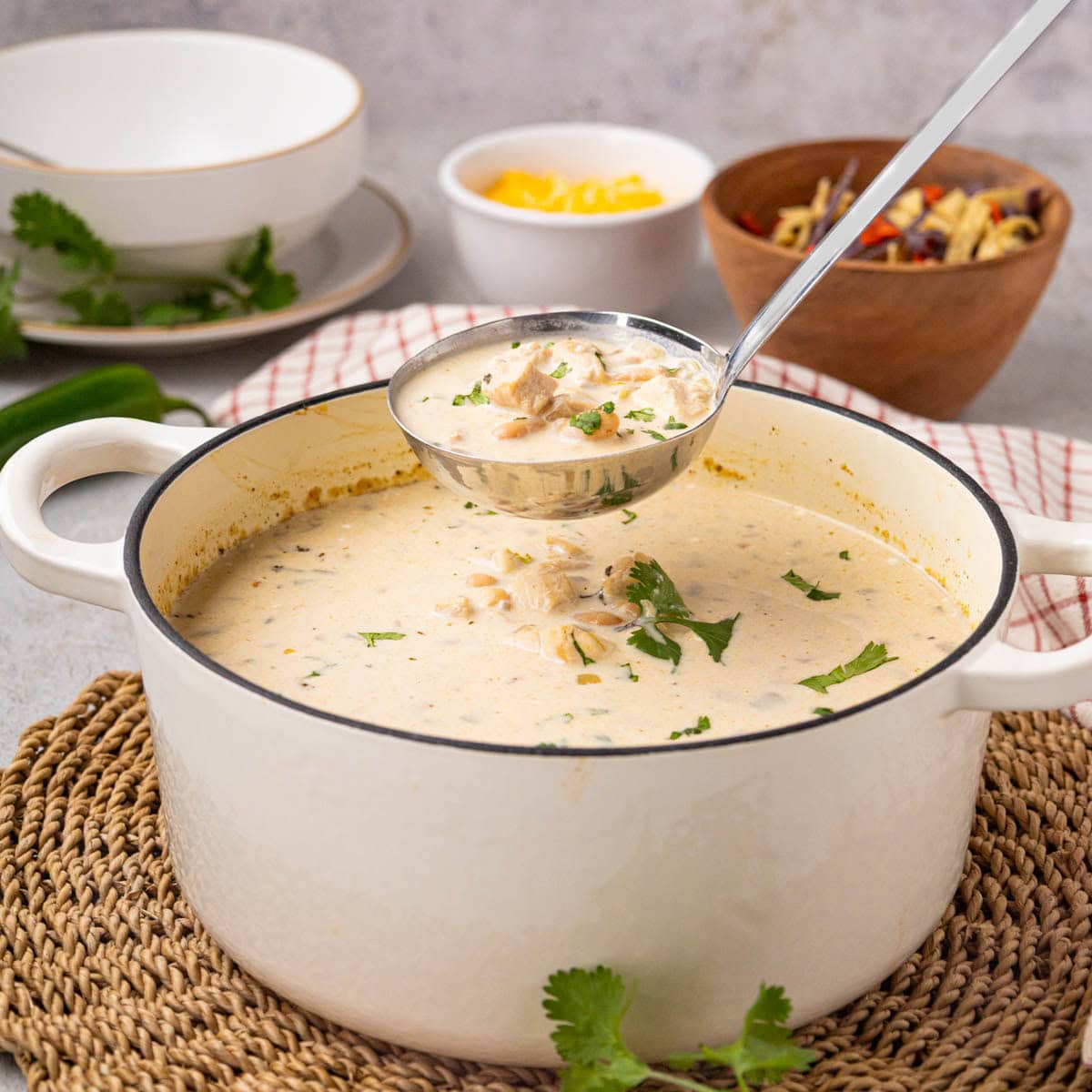 A ladle removing a scoop of white chicken chili from a white dutch oven.