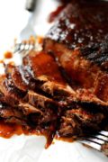 a closeup of this slow cooker beef brisket sliced with sauce and a fork in the background