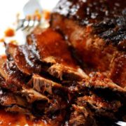 a closeup of this slow cooker beef brisket sliced with sauce and a fork in the background