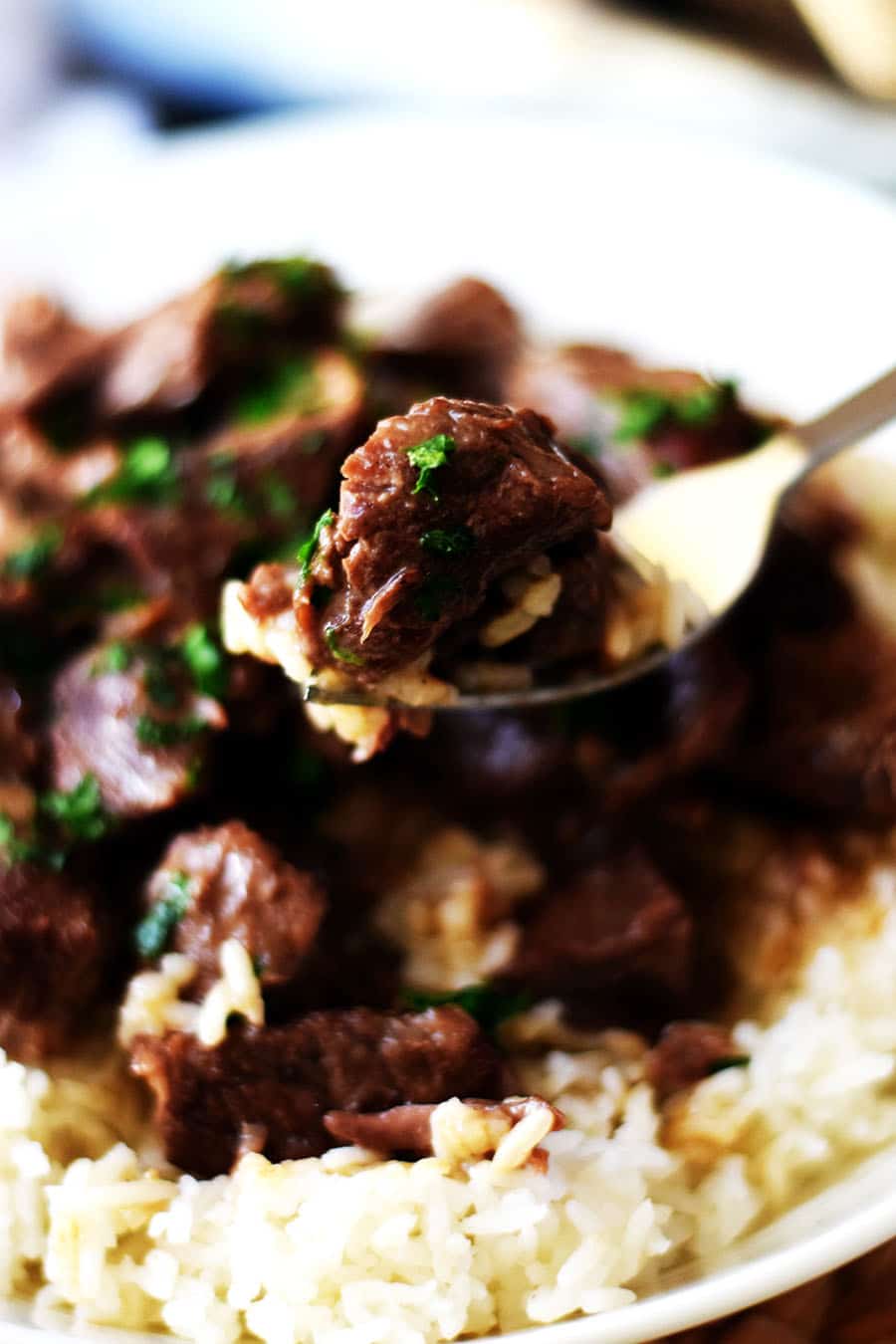 a closeup of a spoonful of these instant pot beef tips aka pressure cooker beef tips with white rice and chopped parsley