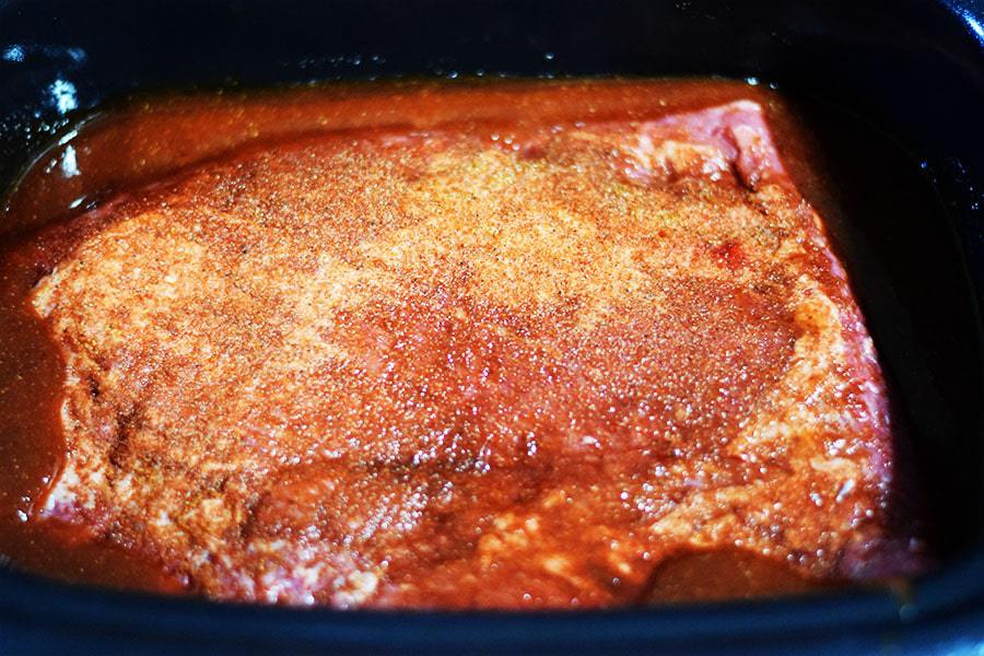 a seasoned beef brisket in sauce inside of a crock pot