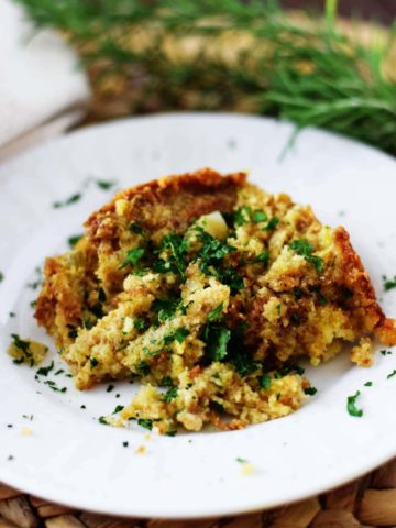 a serving of this crock pot cornbread dressing on a white plate garnished with chopped parsley