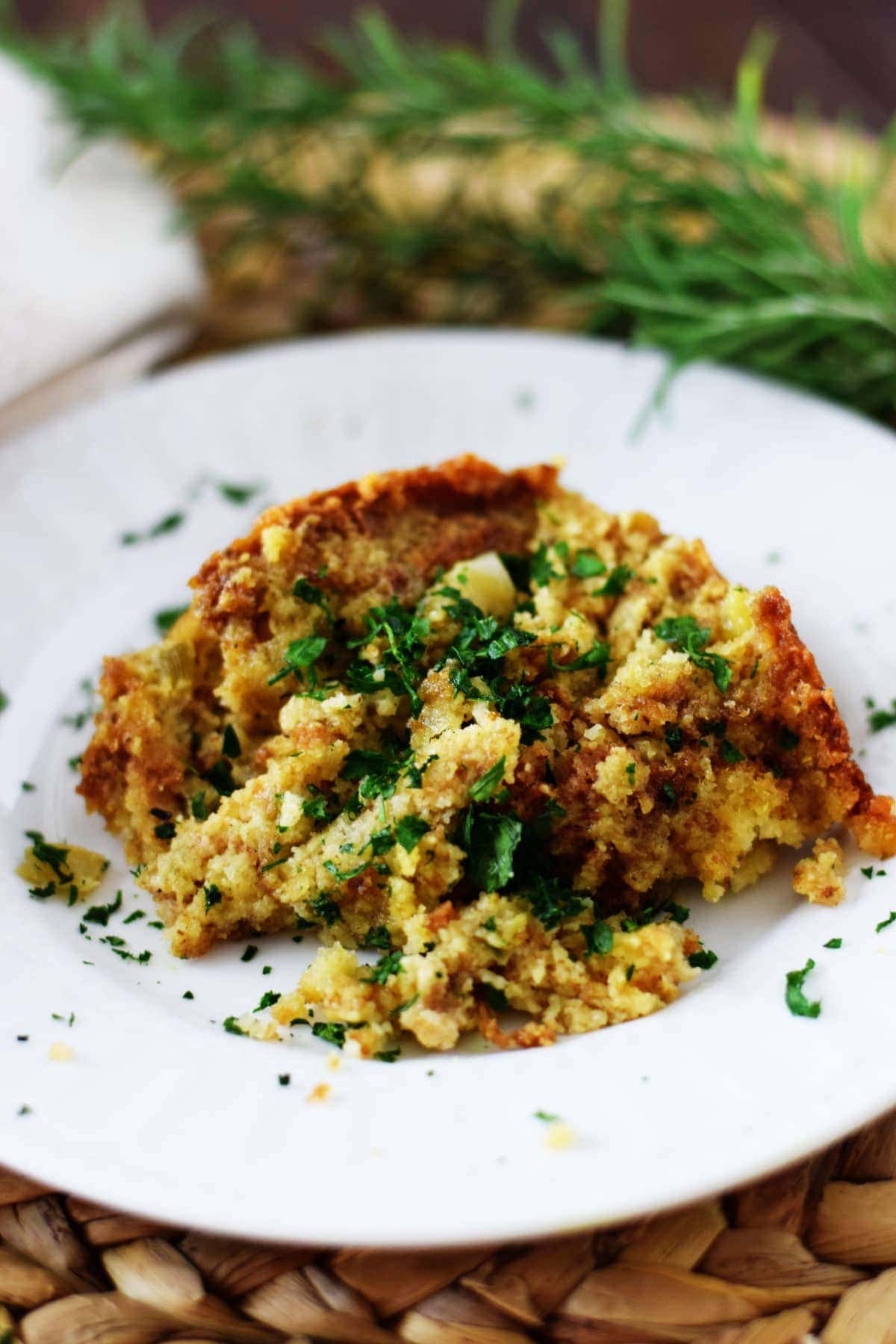 a serving of this crock pot cornbread dressing on a white plate garnished with chopped parsley