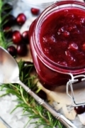 A close up of this festive crock pot cranberry sauce in a festive jar with a silver spoon and pine needles as decoration