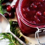 A close up of this festive crock pot cranberry sauce in a festive jar with a silver spoon and pine needles as decoration