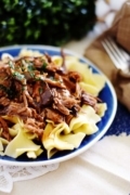 A close up of this crock pot Mississippi pot roast served in a blue bowl over egg  noodles