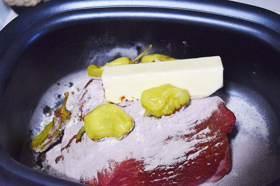 the rump roast, pepperochinis, butter, and dry ingredients inside of a crock pot to make this slow cooker mississippi pot roast recipe