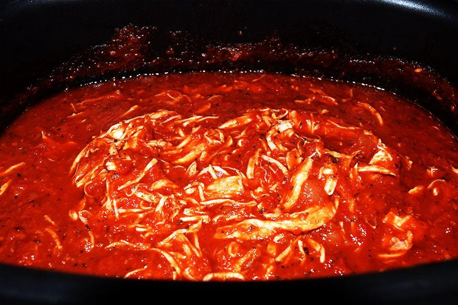 a closeup of the marinara sauce and shredded chicken inside of the slow cooker for this crock pot chicken parmesan penne pasta