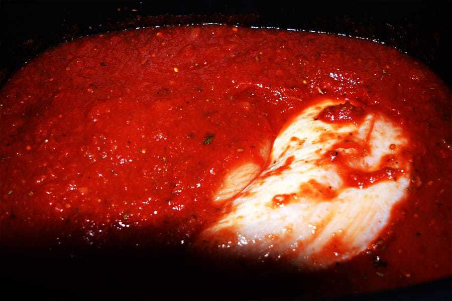 a closeup of the marinara sauce and raw chicken inside of the slow cooker for this crock pot chicken parmesan penne pasta