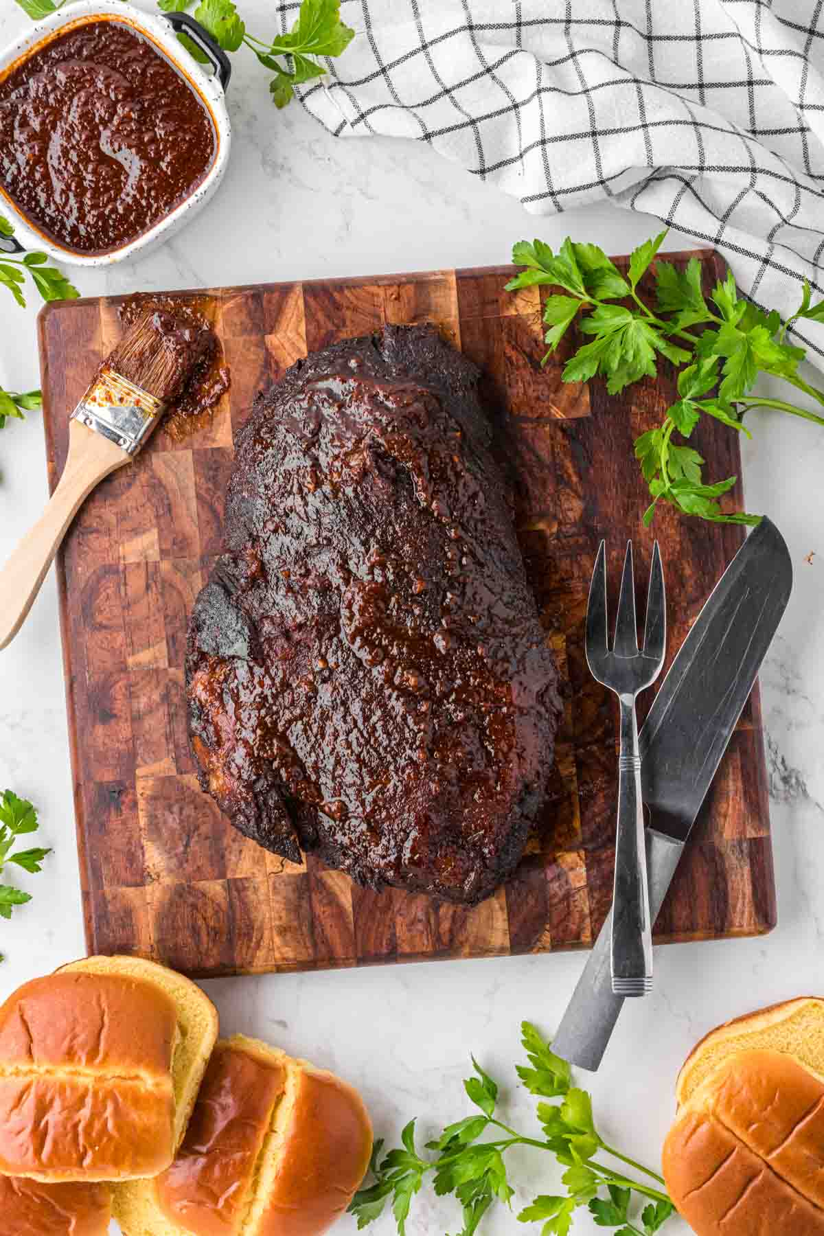 A whole slow cooked beef brisket with bbq sauce on a wooden cutting board.