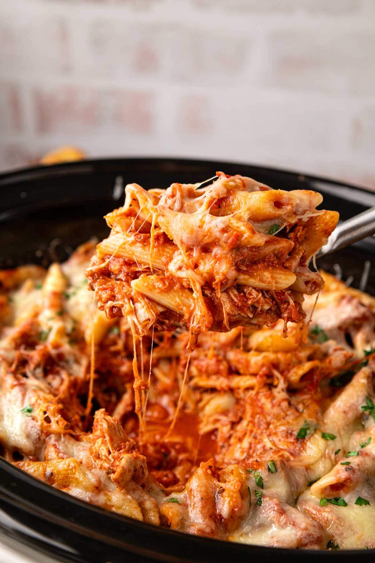 A spoon removing a scoop of slow cooker chicken parmesan pasta from the crock pot.