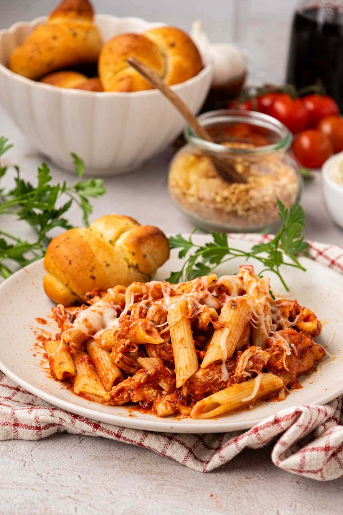 Crock Pot Chicken Parmesan Penne Pasta A plate of crockpot chicken parmesan pasta with a garlic bread knot on a white plate.