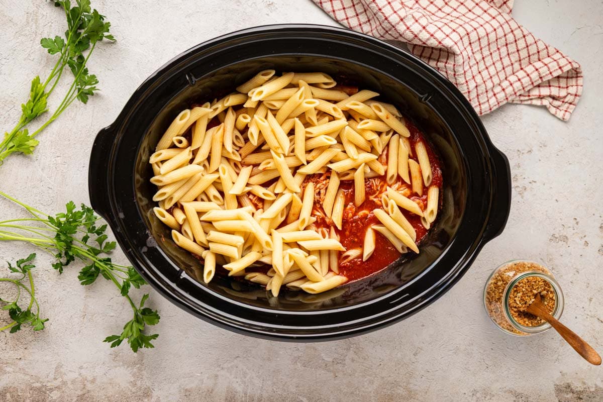 Drained penne pasta added to slow cooker with chicken and sauce.