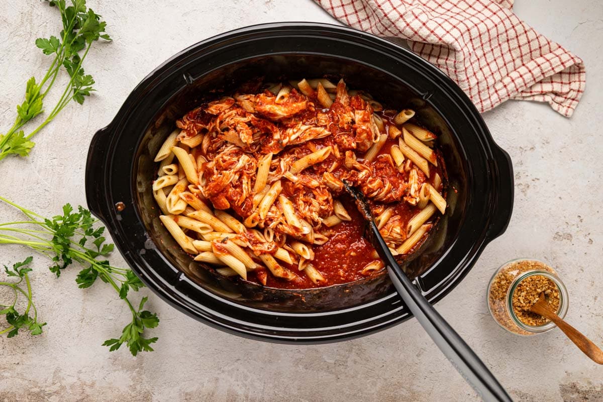 Pasta stirred in the slow cooker to combine with chicken and sauce.