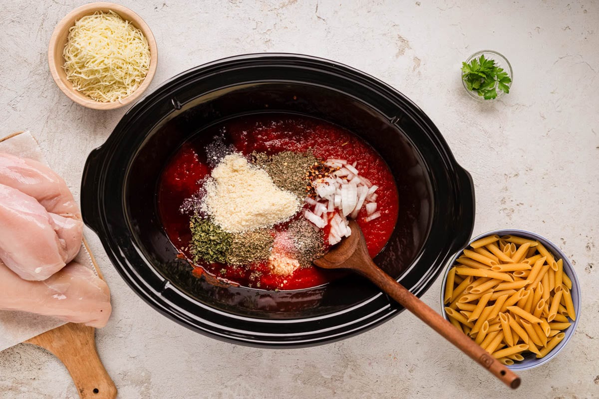 Crushed tomatoes added to a slow cooker with spices and cheese and onions needed to make the sauce.