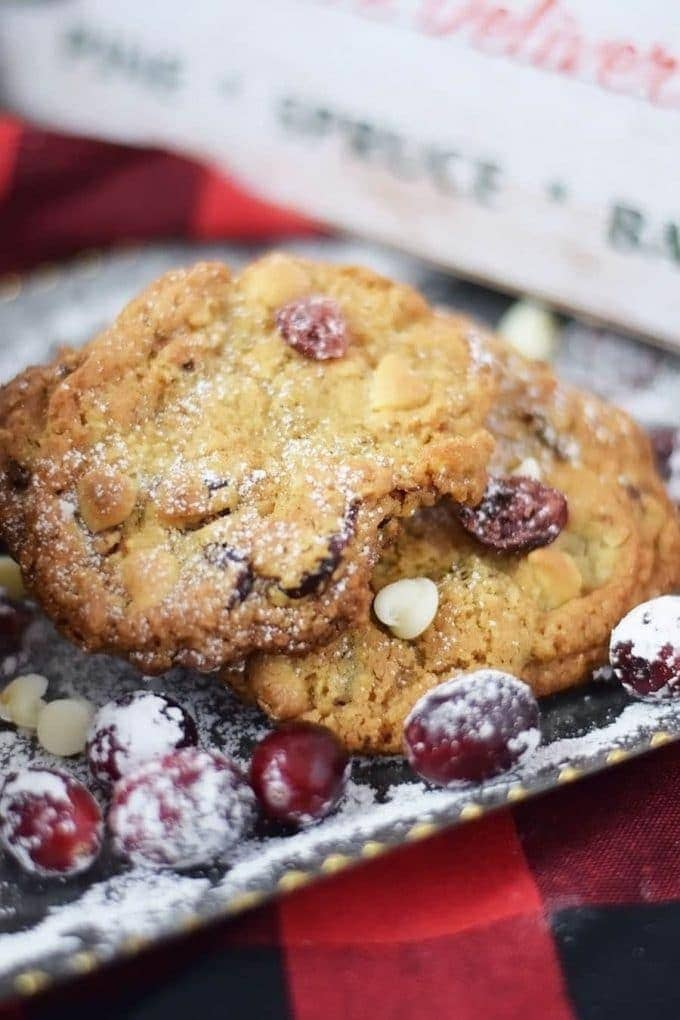 a couple candied cranberry walnut cookies on a serving tray with fresh cranberries and powdered sugar