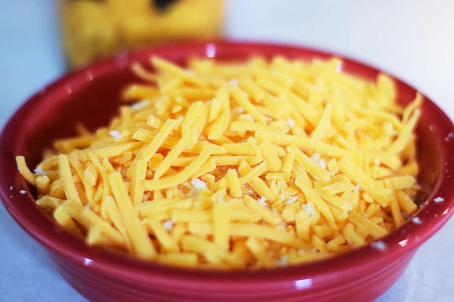 a red bowl filled with grated cheddar cheese