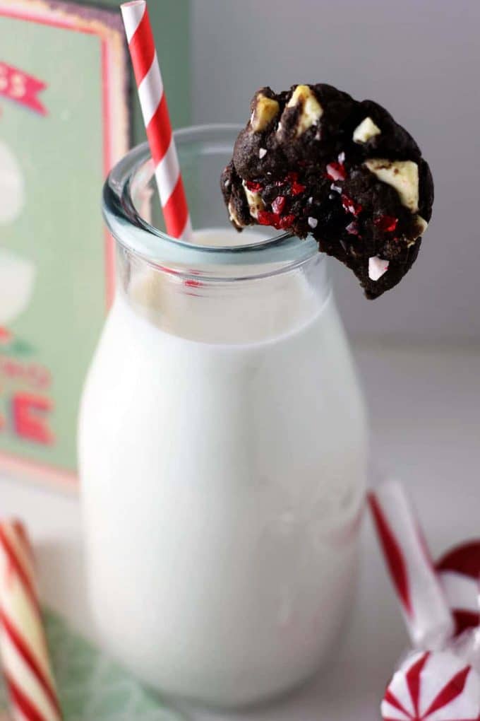 a chocolate oreo peppermint cake mix cookies placed on the rim of a glass milk jug with a red and white straw