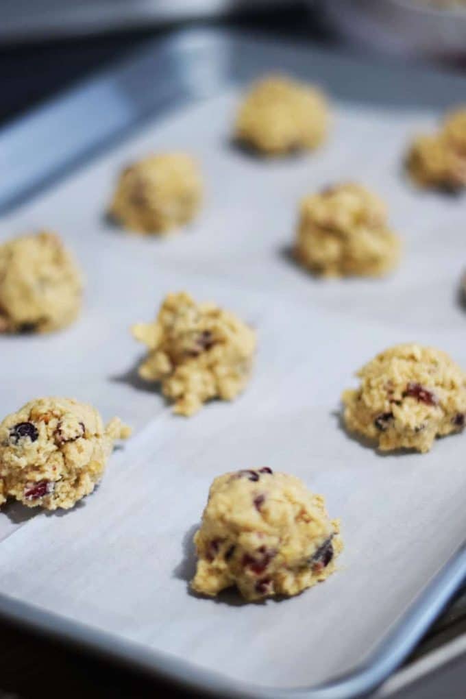 balls of raw candied cranberry walnut oatmeal cookie dough on a lined baking sheet 