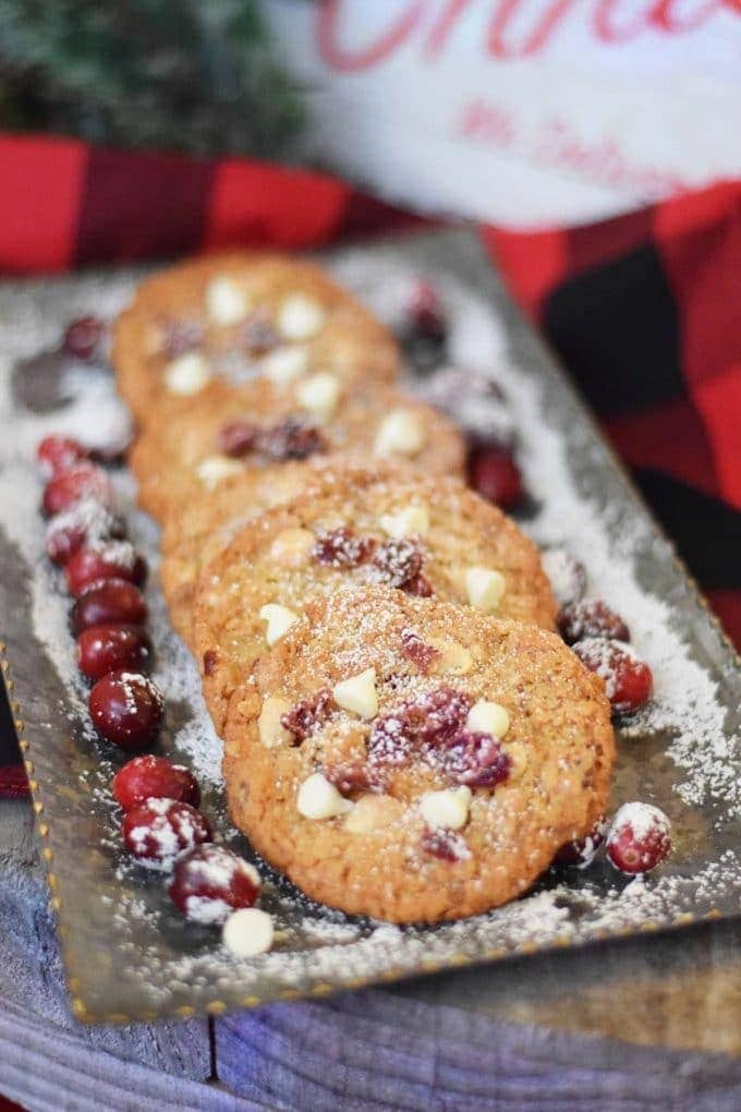 several candied cranberry walnut oatmeal cookies on a serving tray garnished with fresh cranberries and powdered sugar
