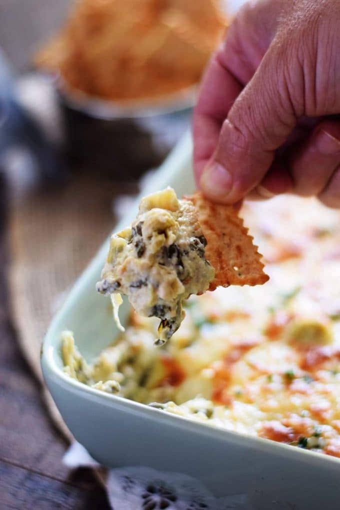 a cracker dipped into the casserole dish filled with this slow cooker spinach and artichoke dip