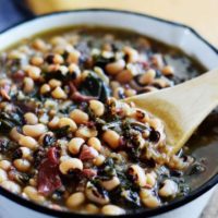 a pot filled with these instant pot black eyed peas and collard greens soup and a wooden spoon
