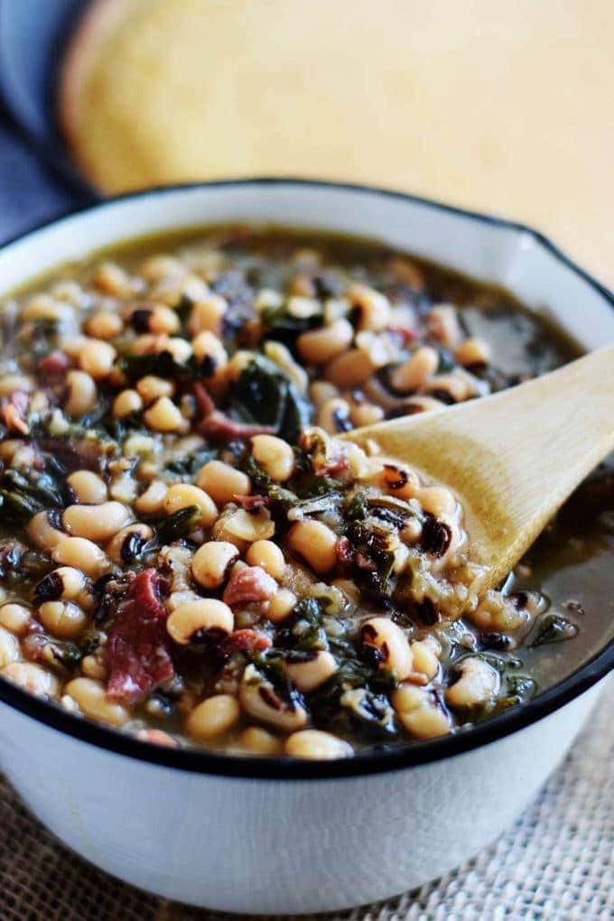 a pot filled with these instant pot black eyed peas and collard greens soup and a wooden spoon