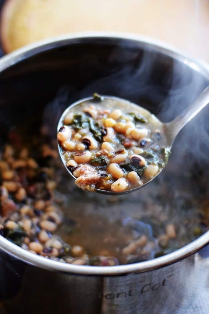 a closeup of a ladle with a serving of this instant pot black eyed pea and collard greens soup