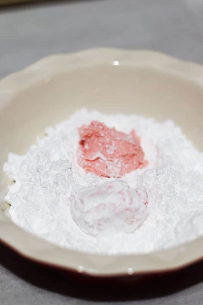 balls of strawberry crinkle cookie dough rolled in powdered sugar before baking