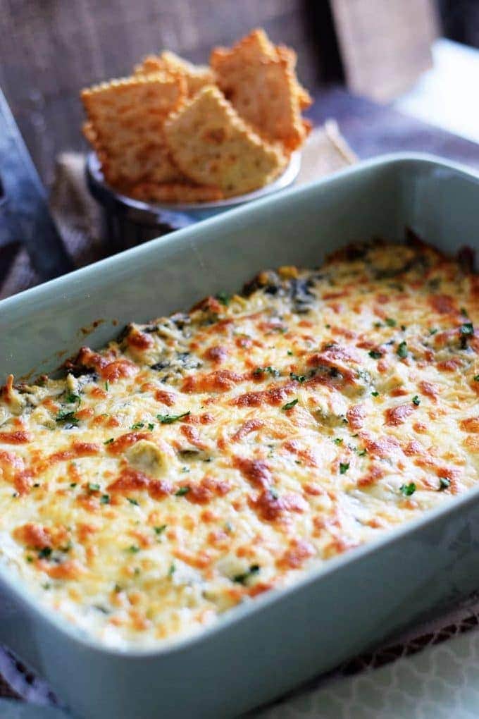 slow cooker spinach artichoke dip in a light blue casserole dish with melted cheese on top