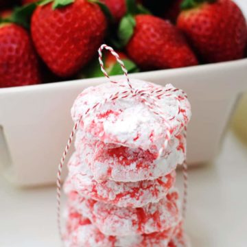 a stack of strawberry crinkle cookies tied together with red and white twine and a basket of fresh strawberries in the background